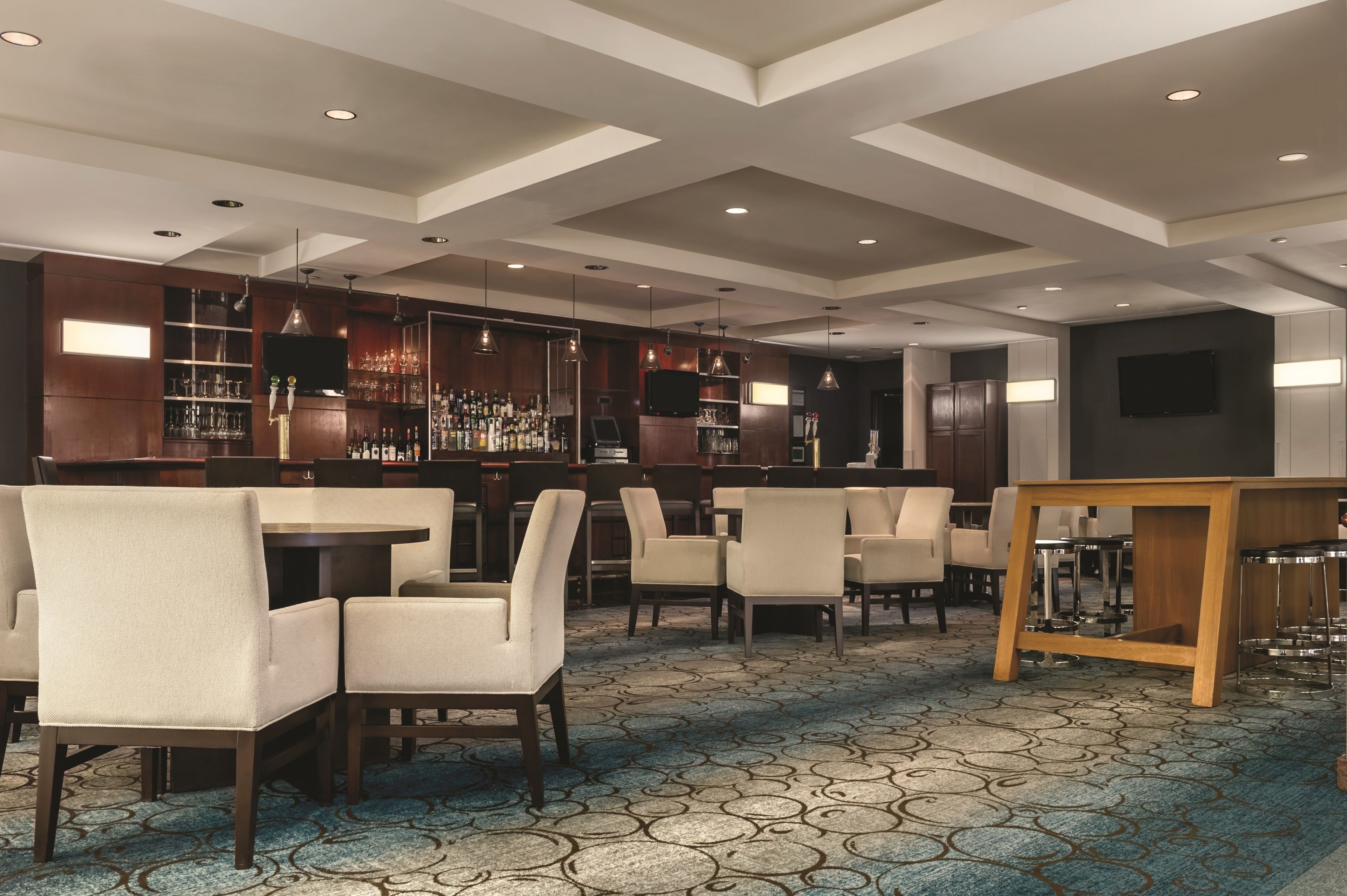 A modern bar area with a high ceiling, recessed lighting, and a patterned carpet.