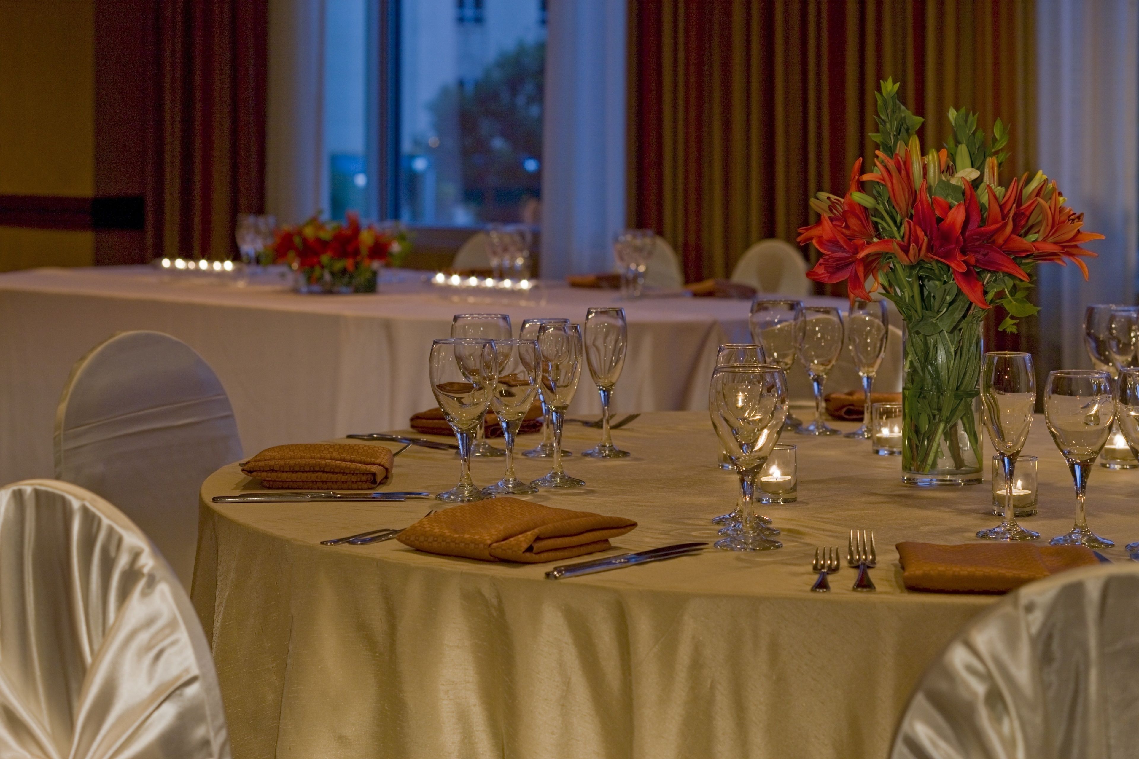 A banquet table set for a formal event with a white tablecloth, multiple wine glasses, and a centerpiece of red flowers.
