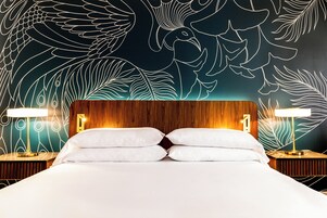 A hotel room with a large bed, two bedside tables with lamps, and a wall with a leaf pattern design.