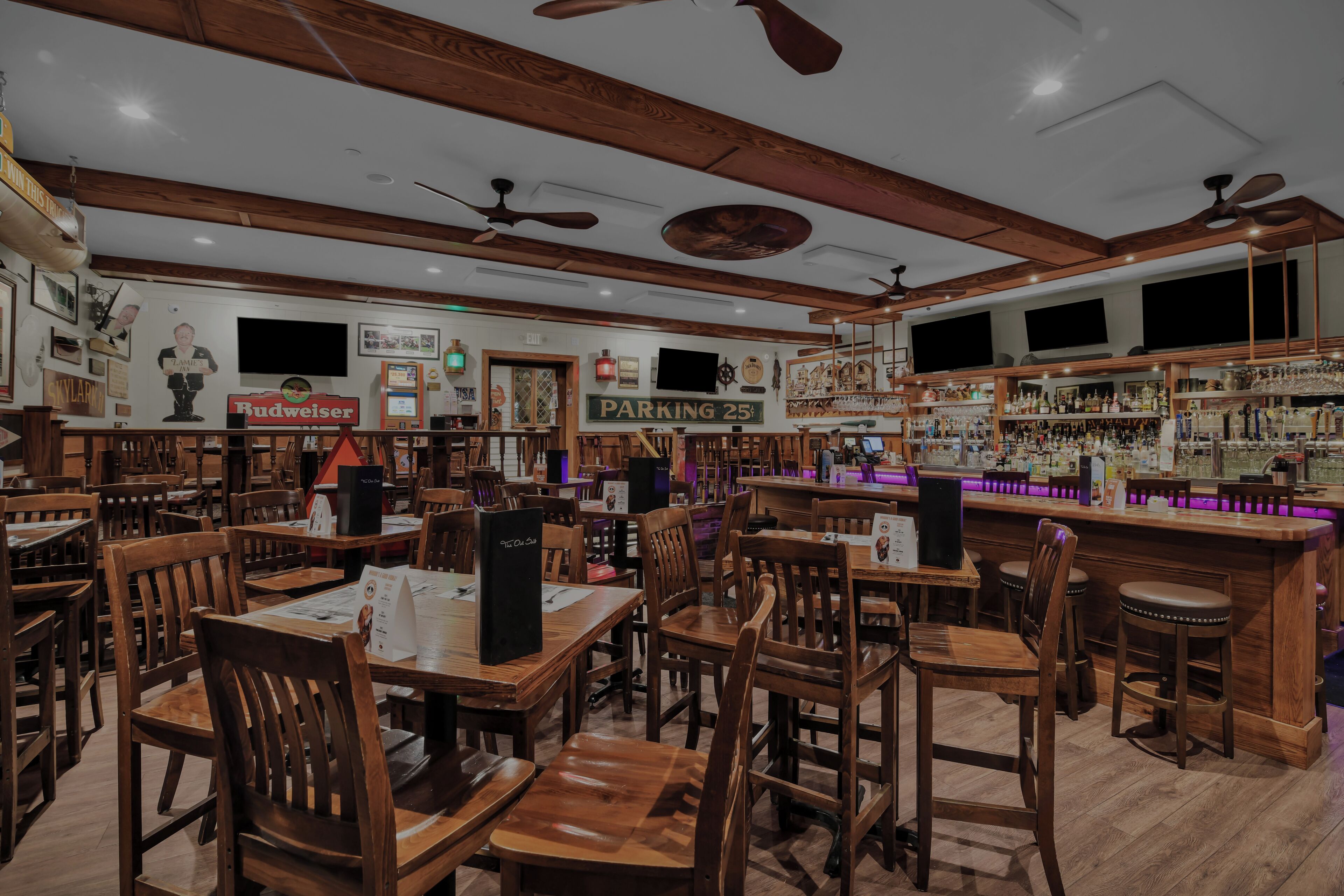 A bar with wooden furniture, a sign for parking, and a Budweiser sign.