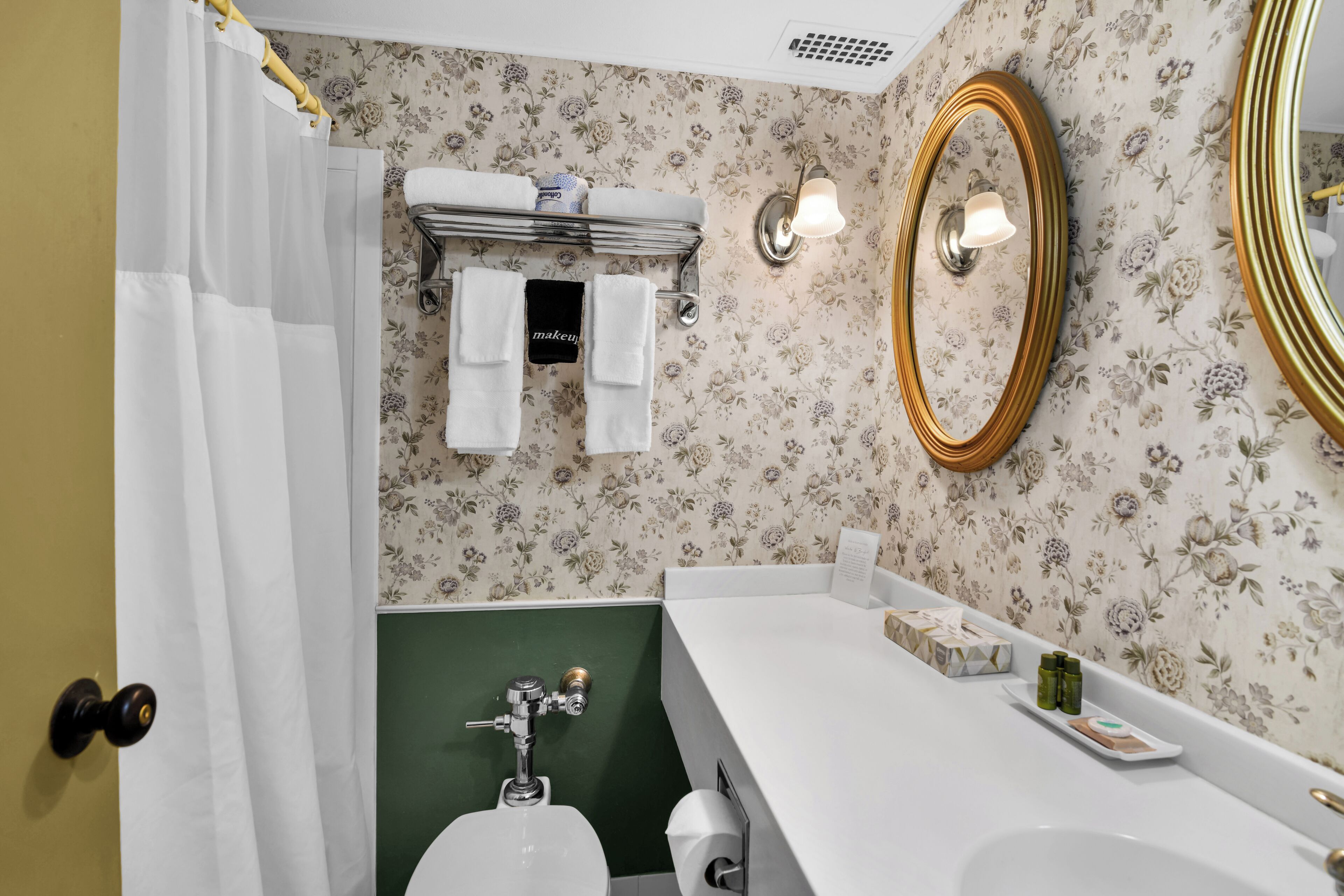 Ein Badezimmer mit Toilette, Waschbecken, Duschvorhang, Handtuchhalter und einem Spiegel.