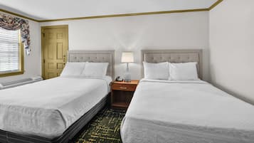 A hotel room with two beds, a bedside table with a lamp, a telephone, and a window with blinds.