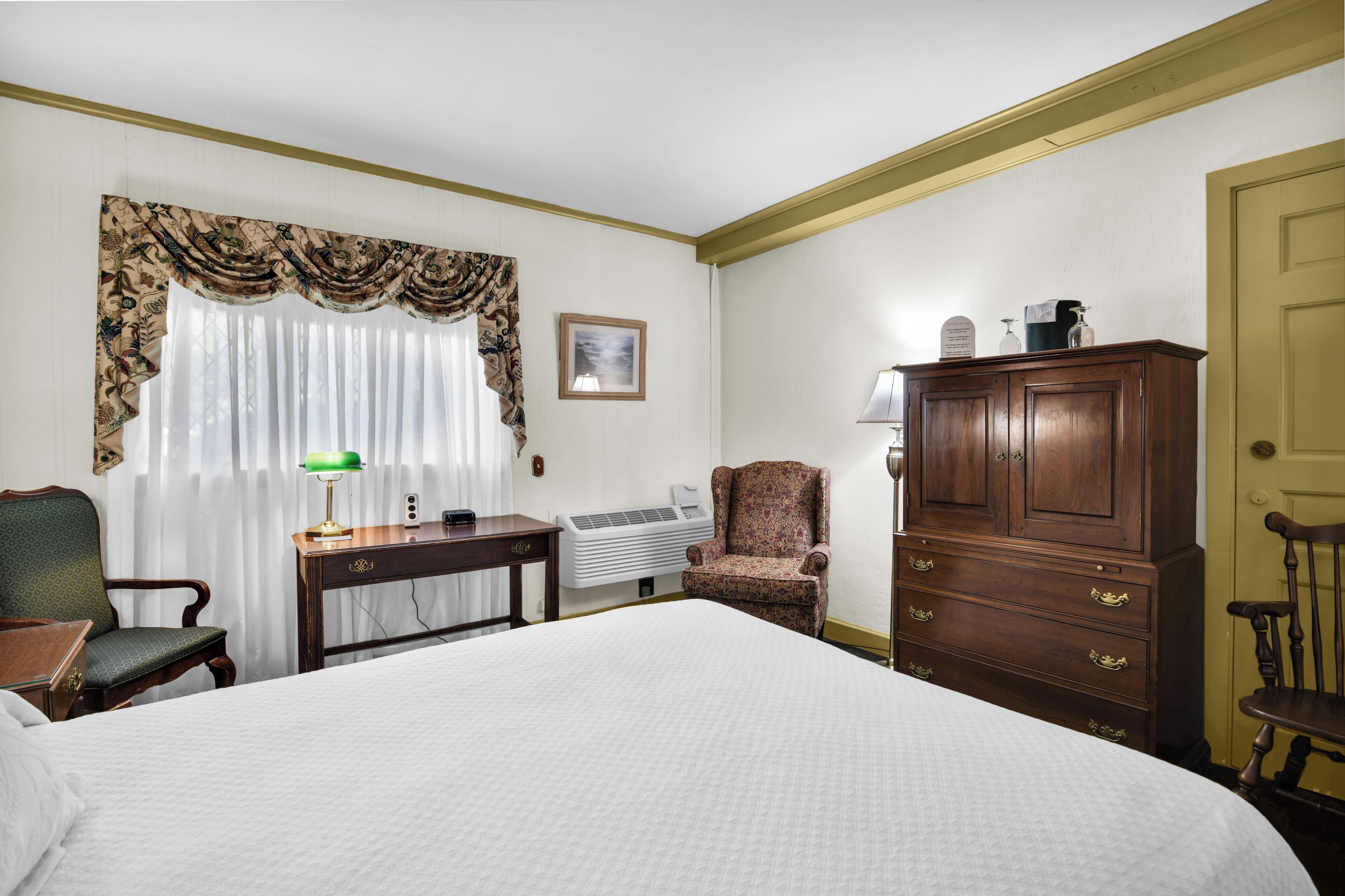 Habitación de hotel con una cama grande, un escritorio con lámpara, una silla, un armario y un radiador.
