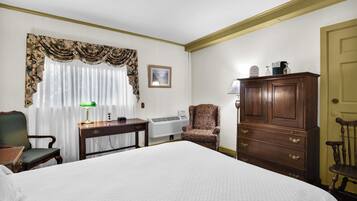 Habitación de hotel con una cama grande, un escritorio con lámpara, una silla, un armario y un radiador.