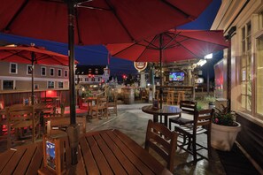 An outdoor seating area with wooden tables and chairs, red umbrellas, and a bar area with a television. - Lamie's Inn and The Old Salt Restaurant (Hampton)