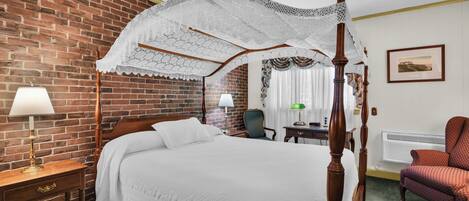 A four-poster bed with a white canopy, a wooden nightstand with a lamp, a chair, and a framed picture on the wall.