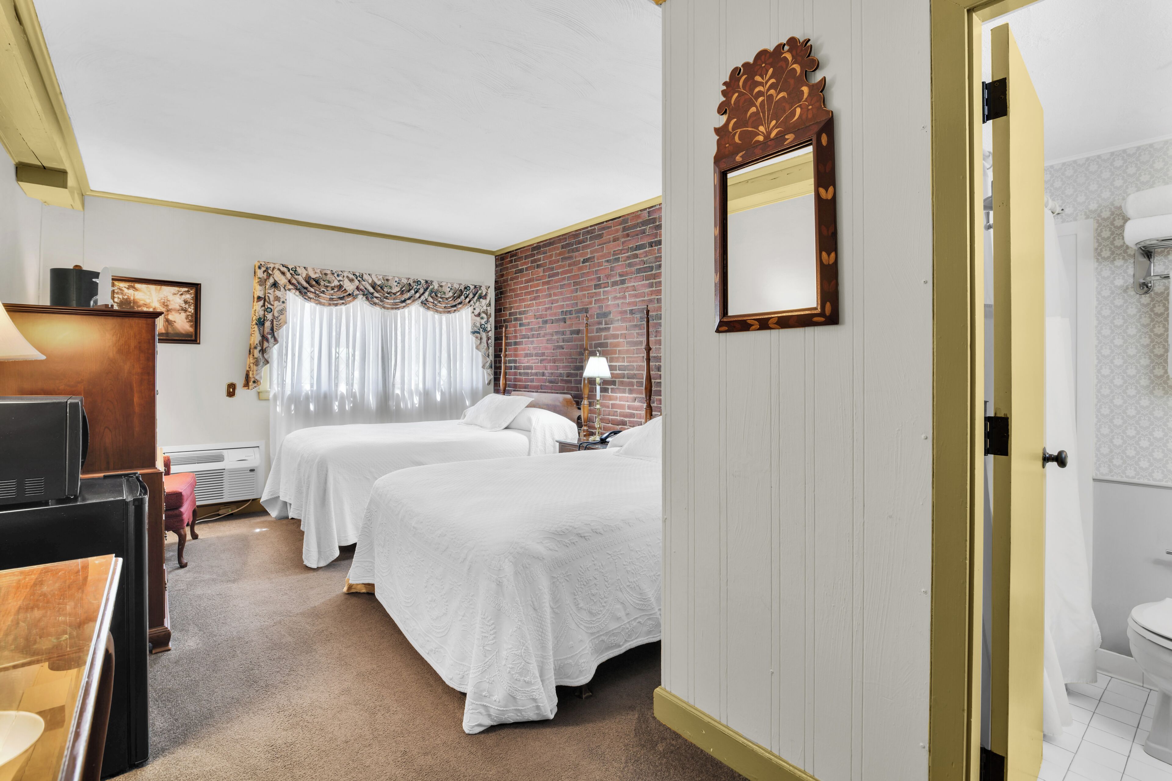 A hotel room with two beds, a desk, a chair, a TV, a mirror, and a bathroom.