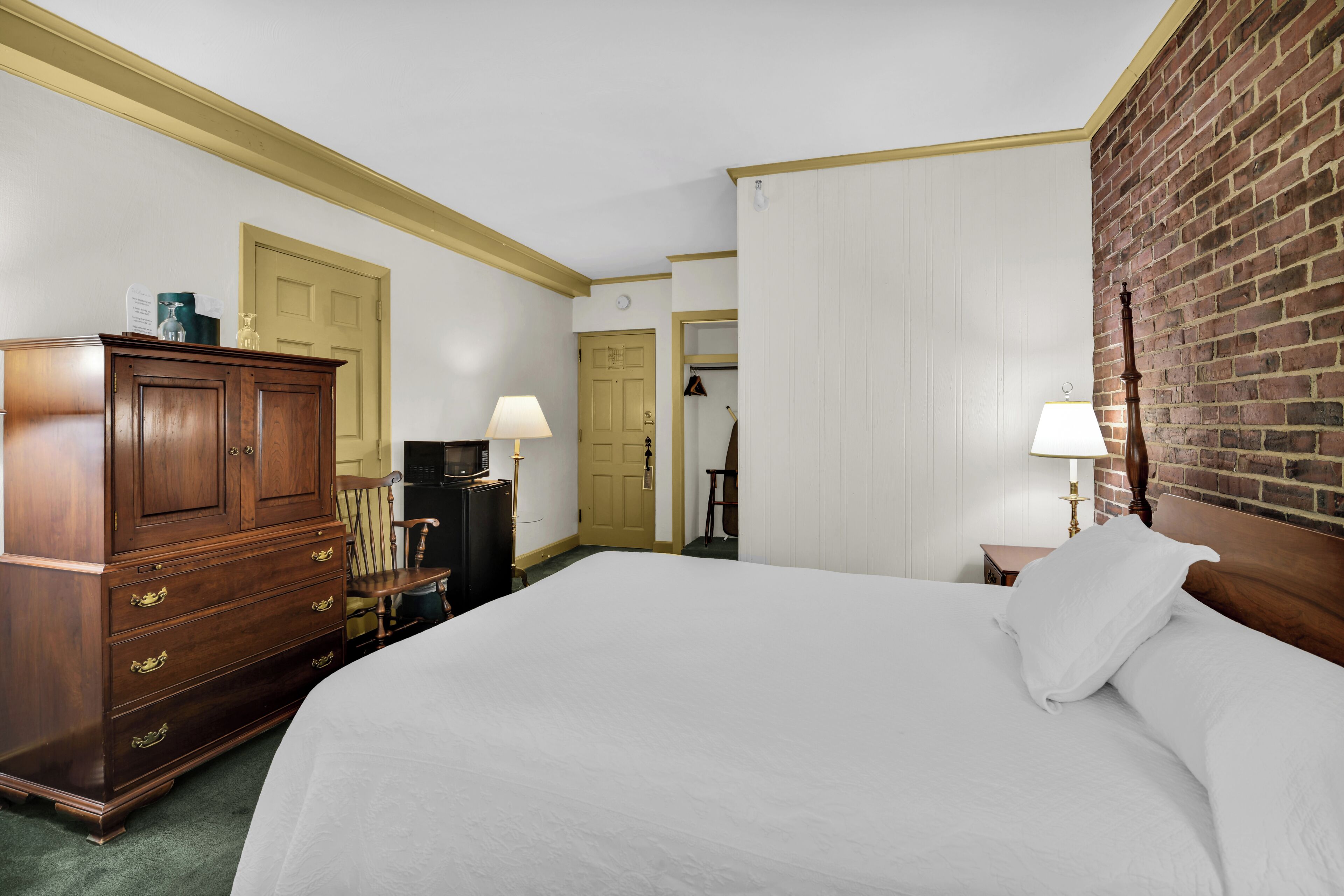 A hotel room with a large bed, wooden dresser, two lamps, and a brick accent wall.