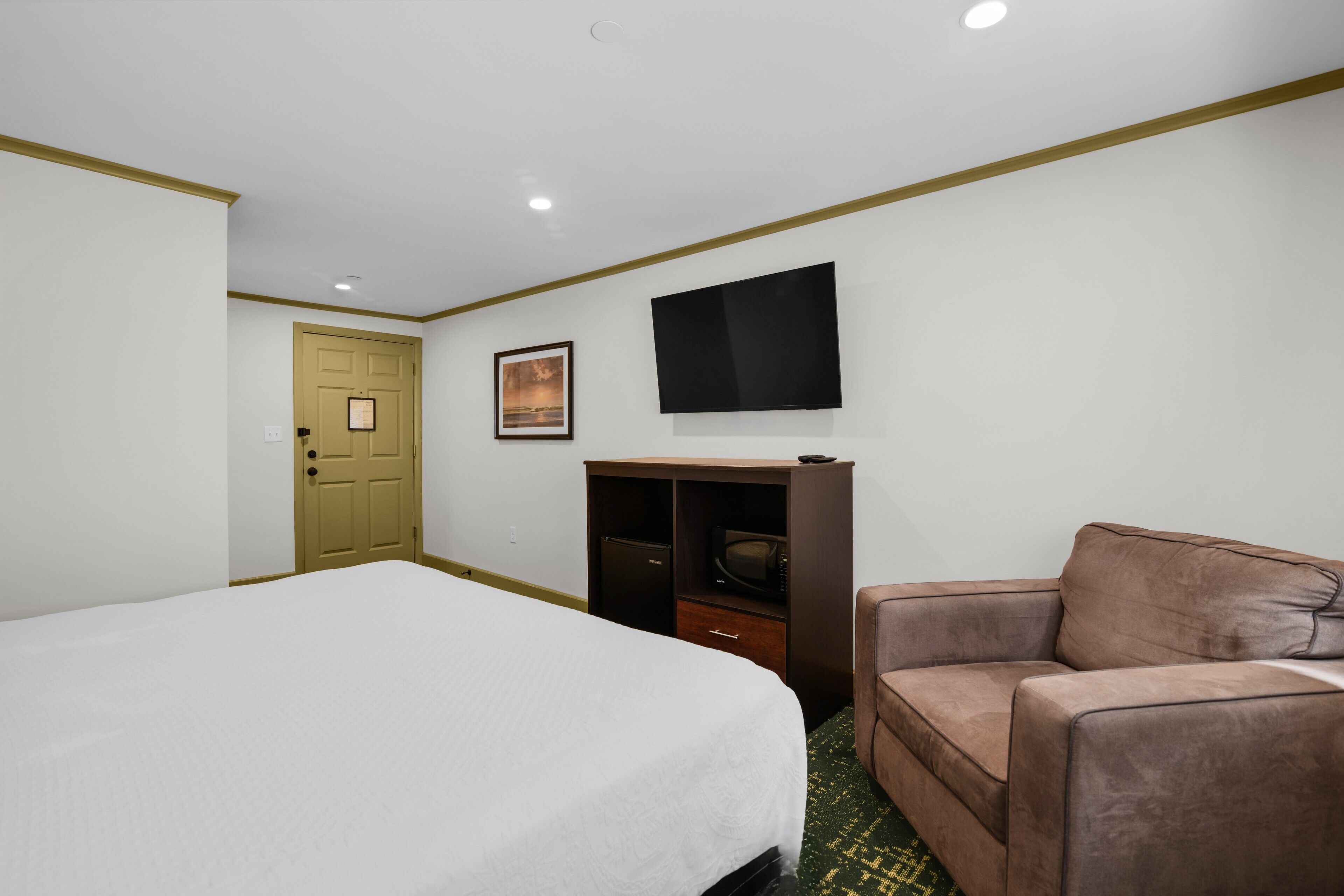 Ein Hotelzimmer mit einem Bett, einem braunen Sofa, einem Fernseher, einer Tür und einem kleinen Schrank.