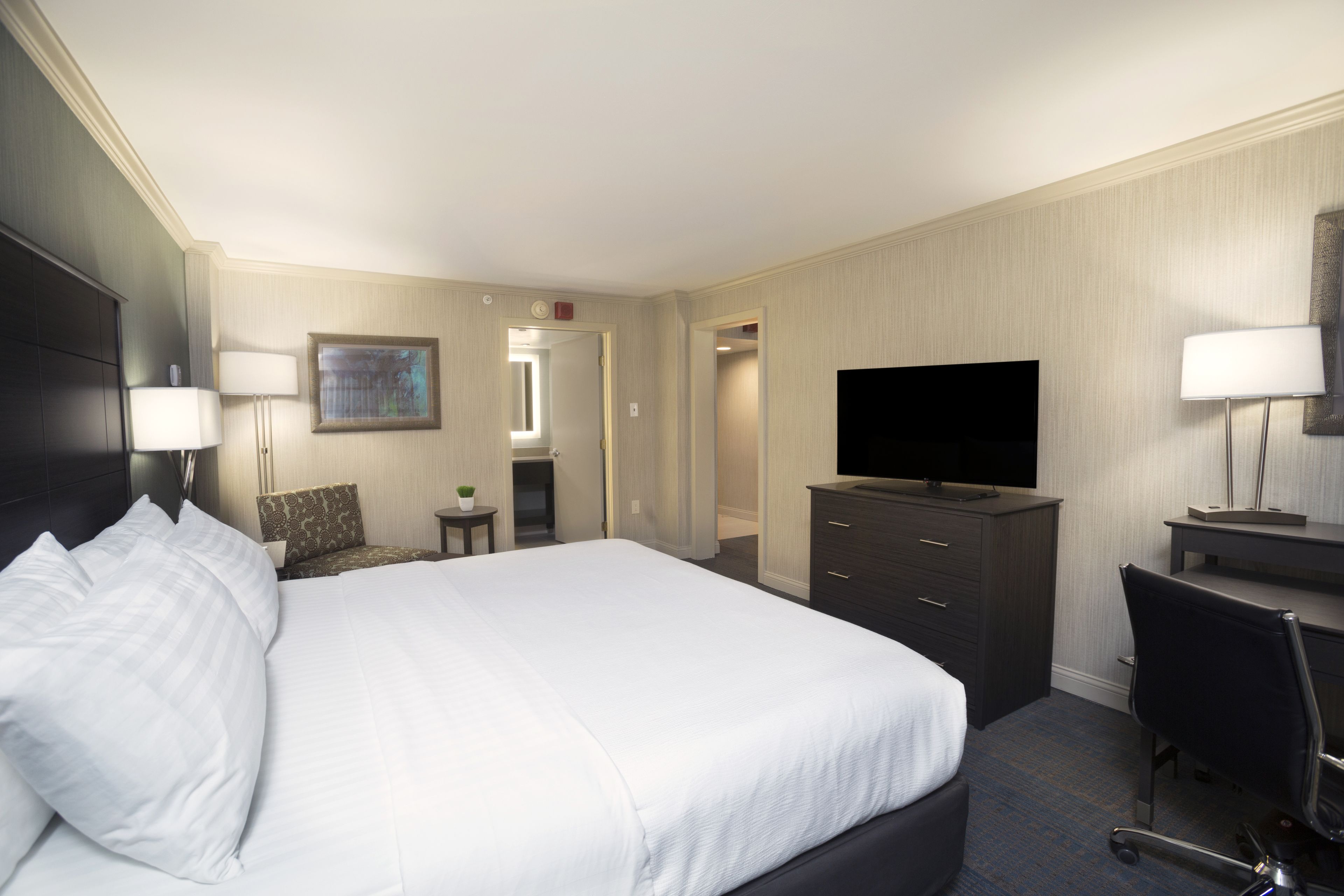 A hotel room with a large bed, a desk, a television, and a chair.