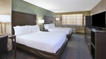 A hotel room with two beds, a desk, a chair, a television, and a window with curtains.