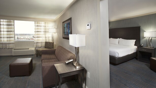 A hotel room with a bed, a sofa, a small table, a lamp, a nightstand, and a window with curtains. - Holiday Inn Columbus Dwtn-Capitol Square by IHG (Columbus)