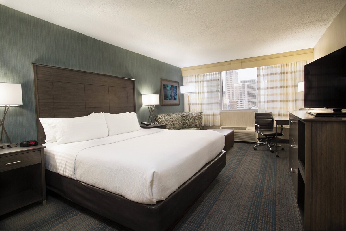 A hotel room with a large bed, a desk, a chair, a television, and a window with curtains.