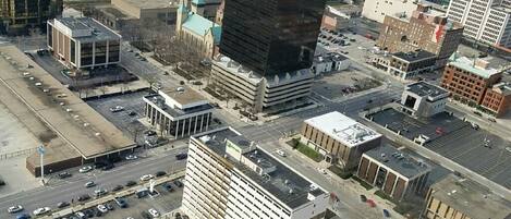 An aerial view of a cityscape with various buildings, including a parking lot with multiple cars and a large building with a distinctive black facade.