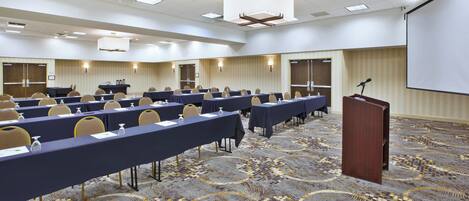 A conference room with rows of tables, chairs, and a podium.