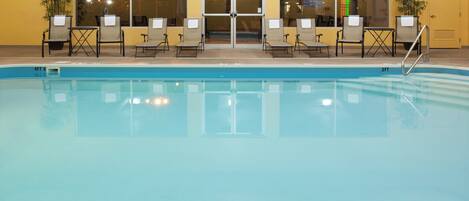 A swimming pool with lounge chairs and a door leading to an indoor area.