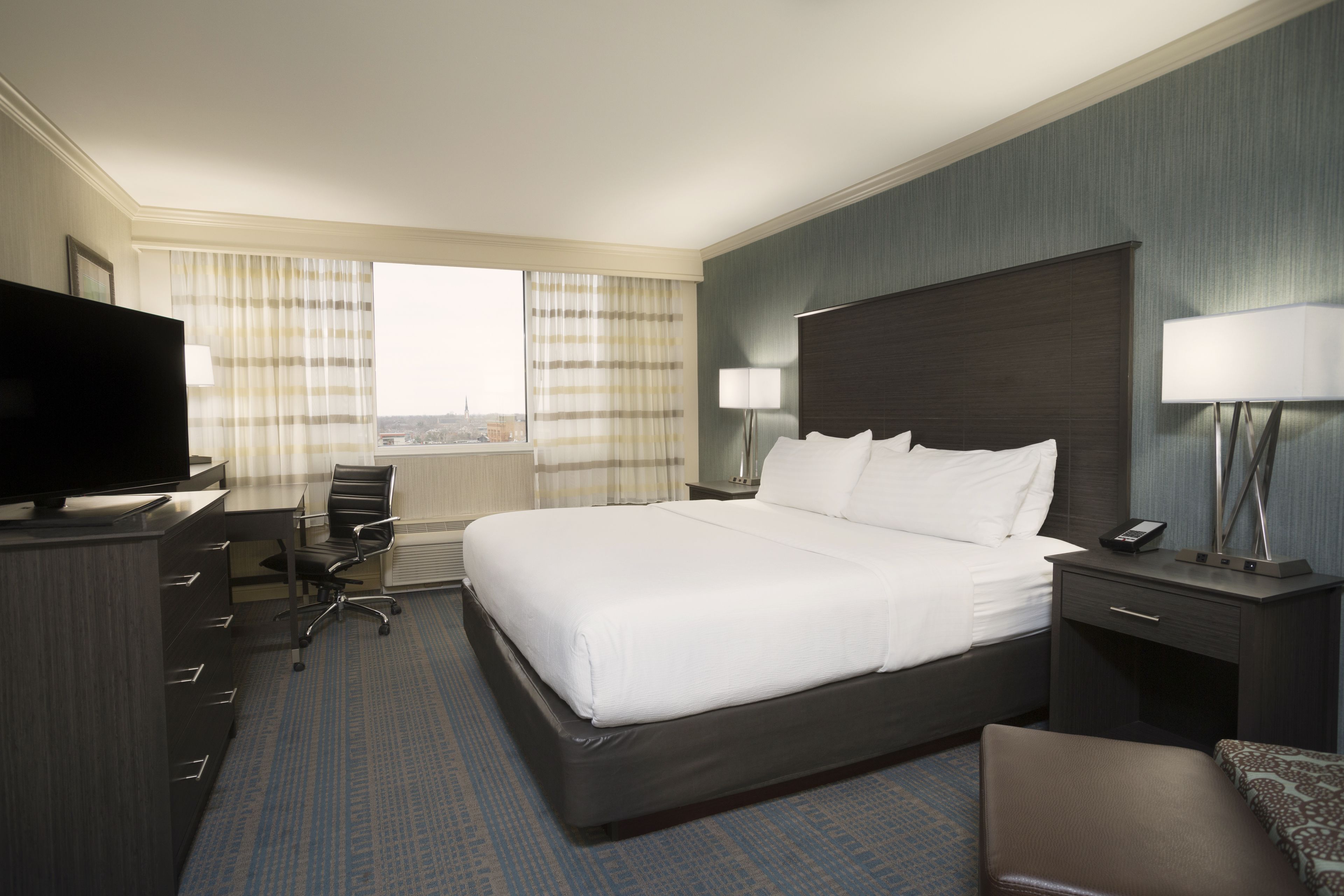 Habitación de hotel con una cama grande, un escritorio con silla, televisor y ventana con cortinas.