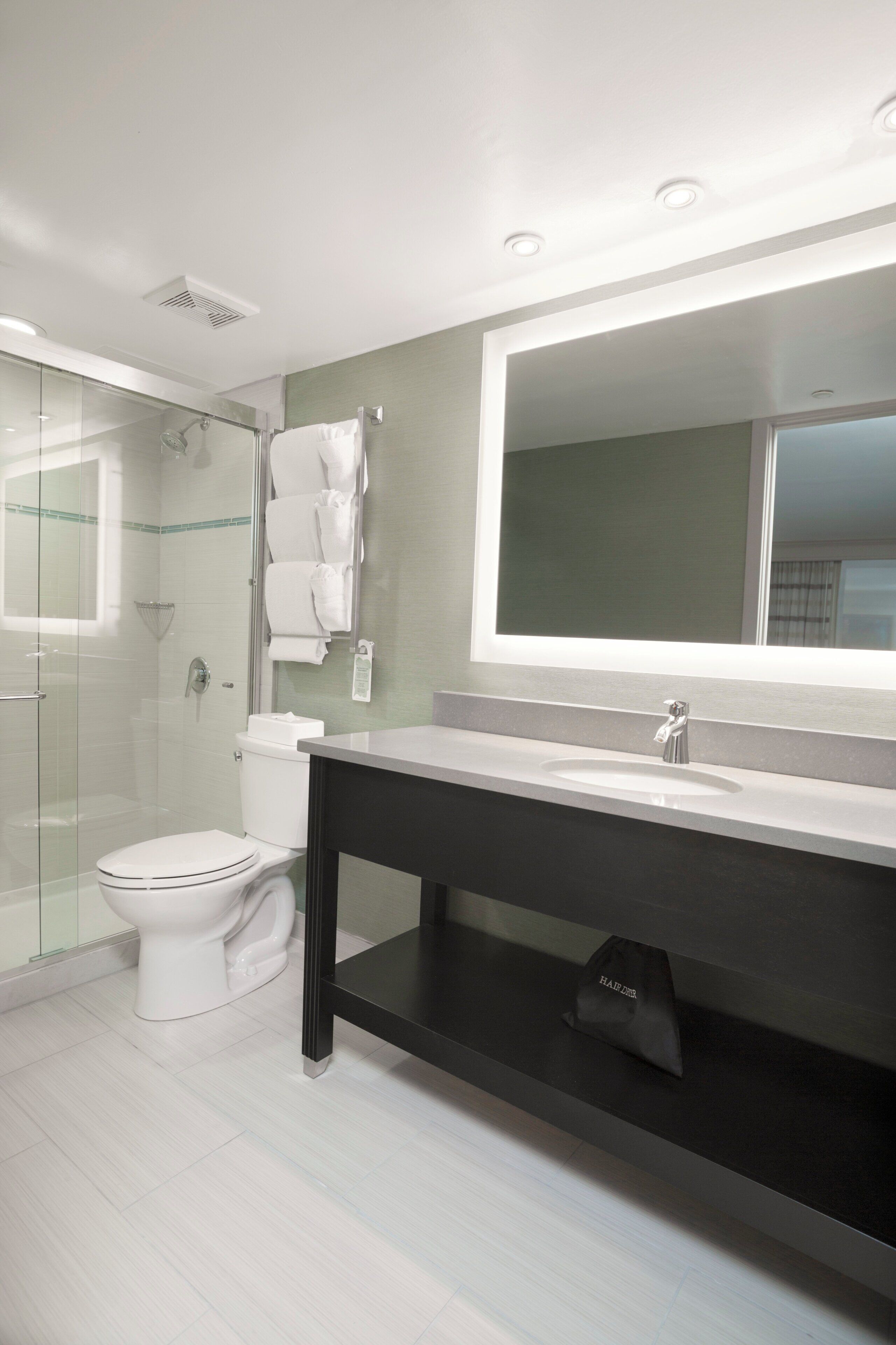 Un baño moderno con cabina de ducha de vidrio, inodoro blanco, tocador con encimera oscura y un espejo grande.