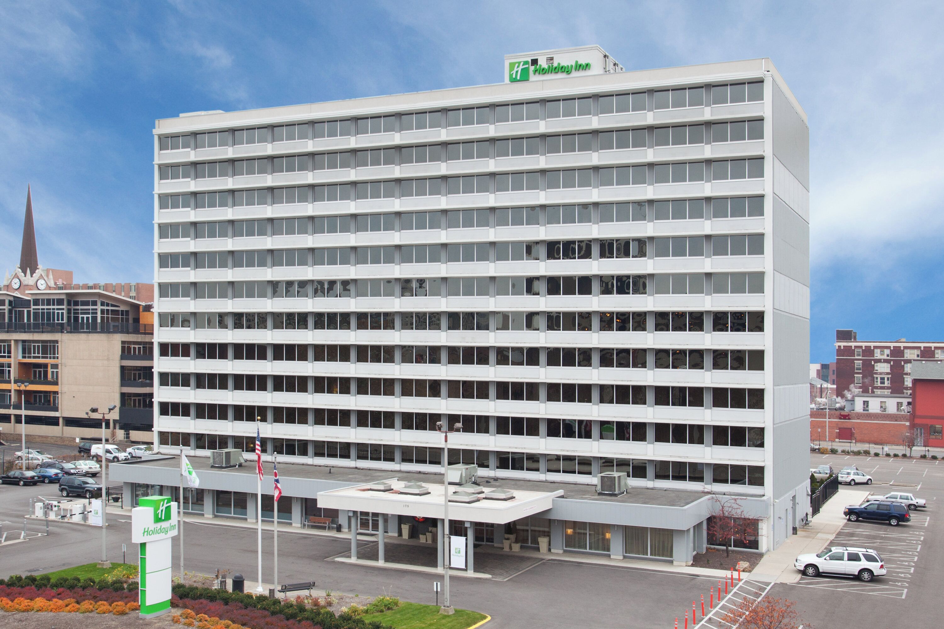 A Holiday Inn hotel building with a modern architectural design, featuring a large parking lot and a prominent entrance.