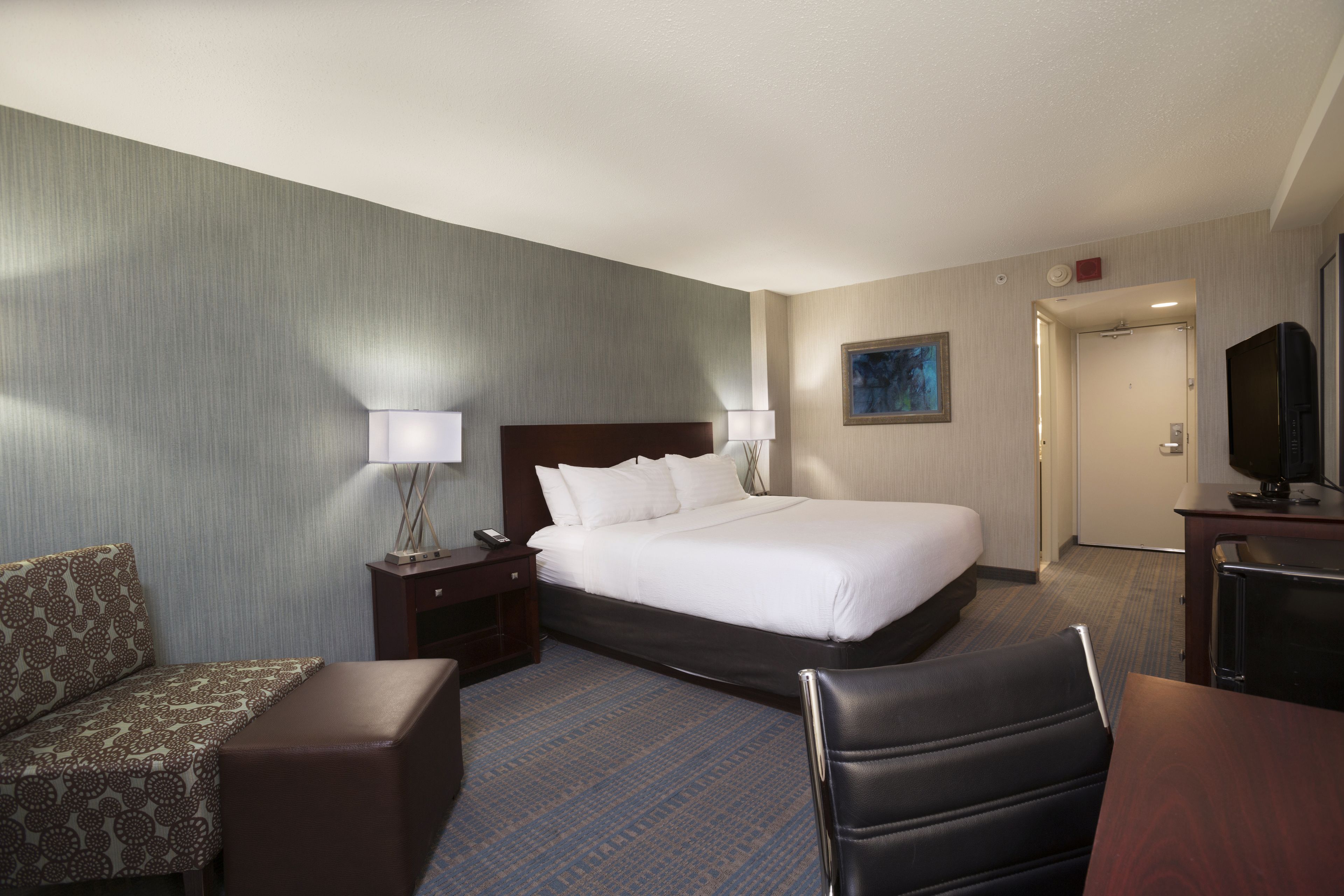 A hotel room with a large bed, a desk with a chair, a sofa, and a television.