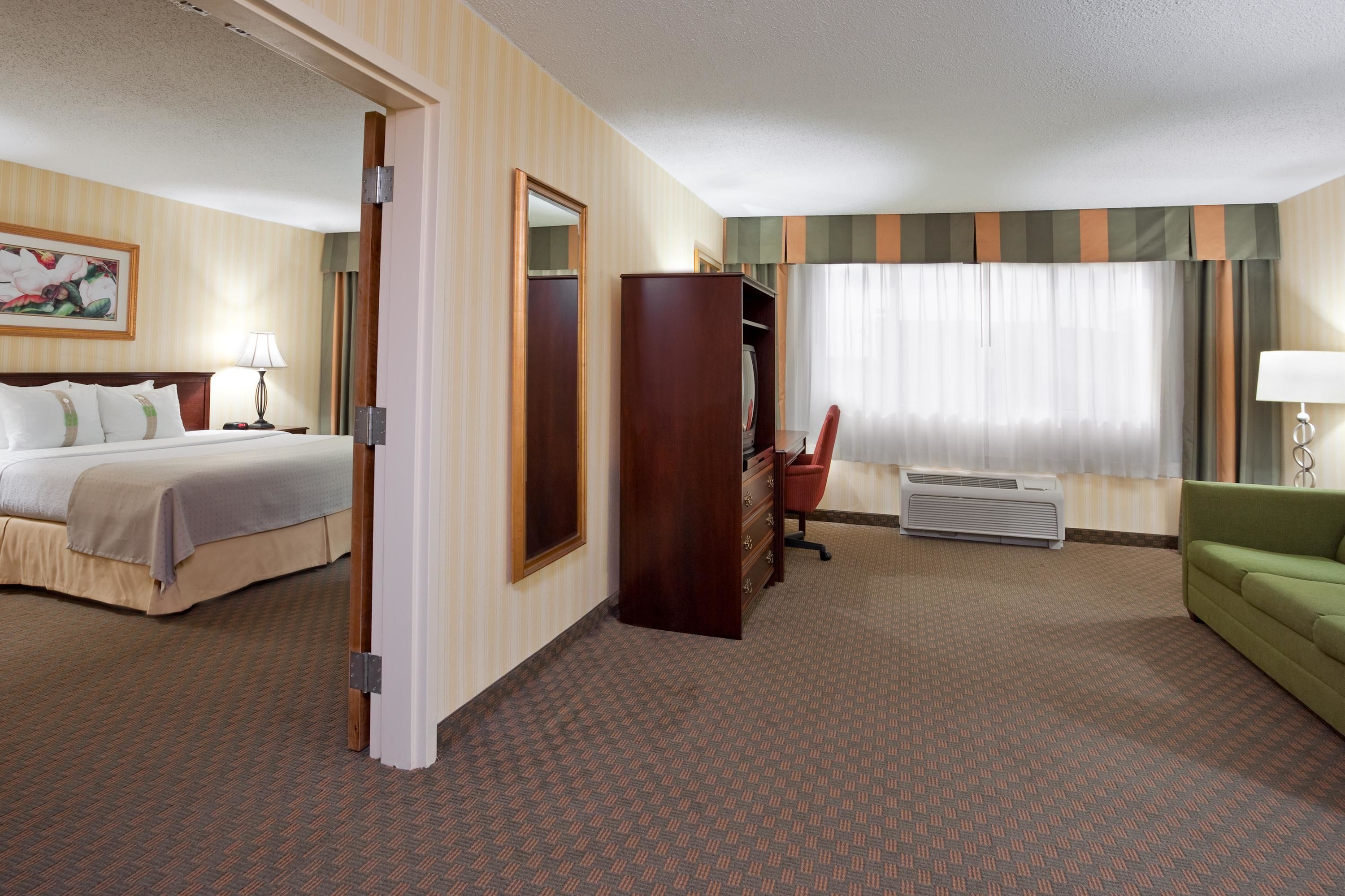 Una habitación de hotel con cama, escritorio, silla, armario y sofá verde.