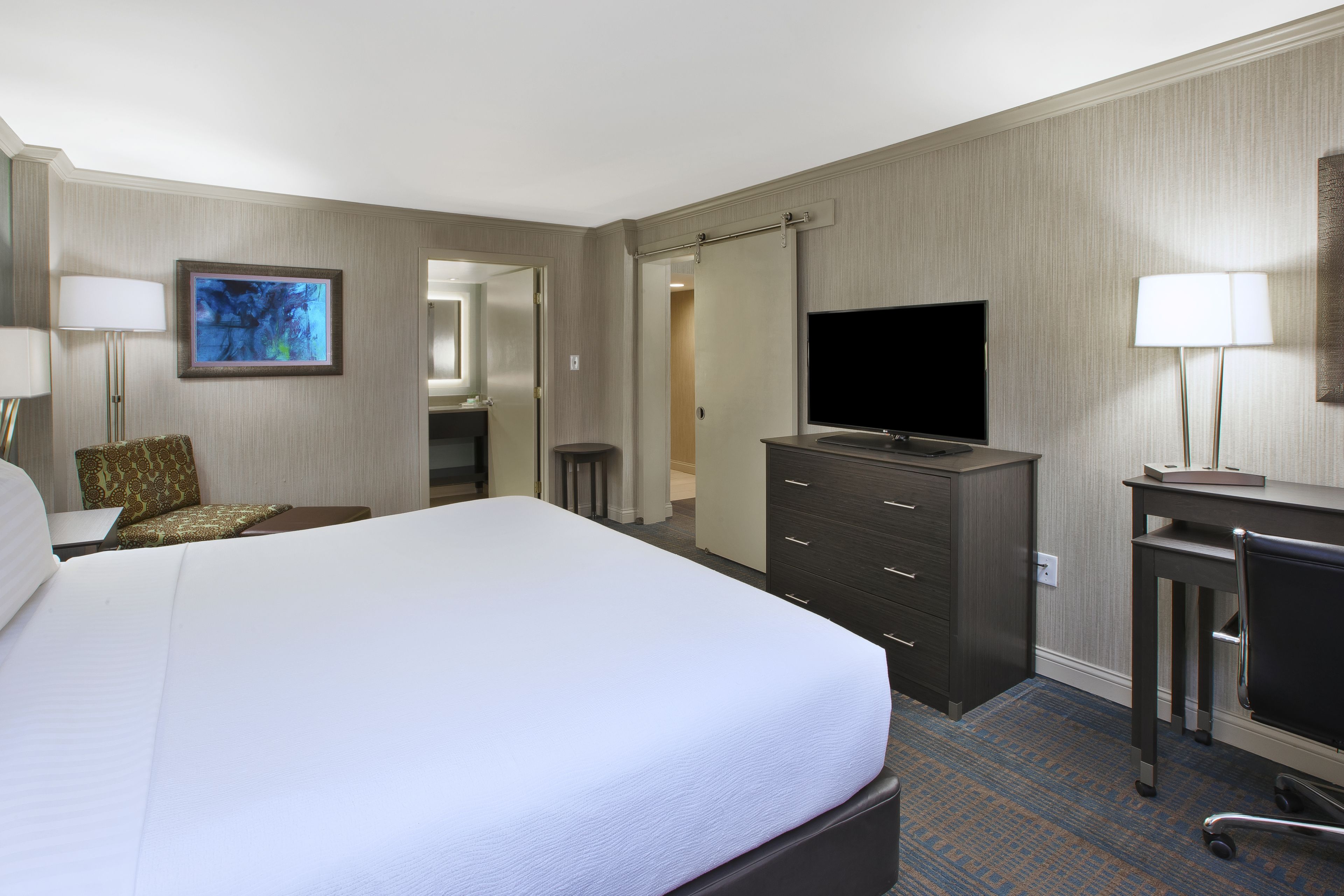 Una habitación de hotel con una cama grande, un escritorio con televisor, un aparador y una silla.