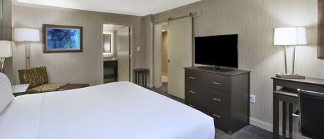 Una habitación de hotel con una cama grande, un escritorio con televisor, un aparador y una silla.