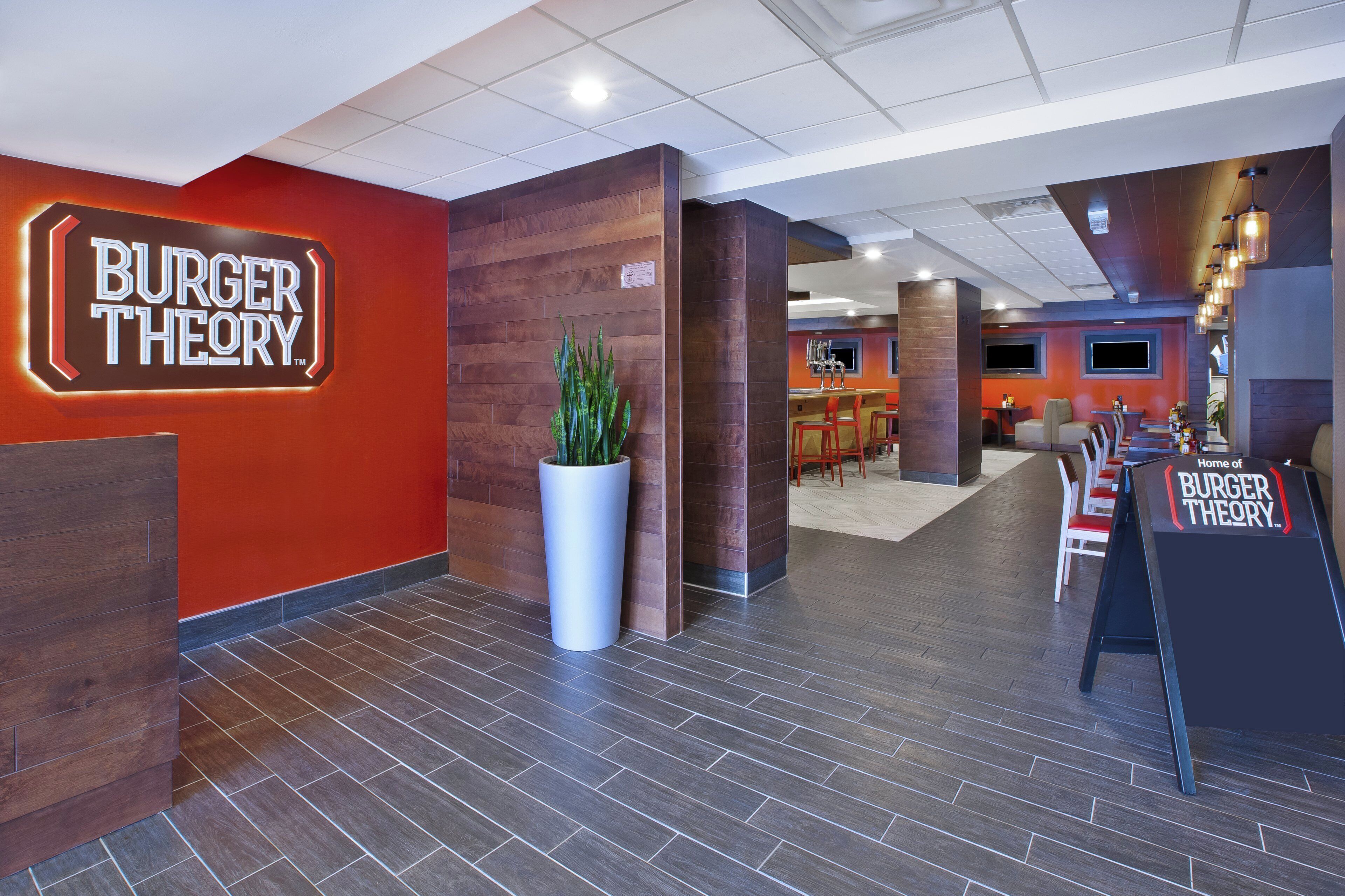 Un interior moderno con un llamativo letrero 'BURGER THEORY', una zona de recepción y un área de estar con bar.