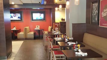 Un restaurante con cabinas y mesas, piso de madera y lámparas colgantes.