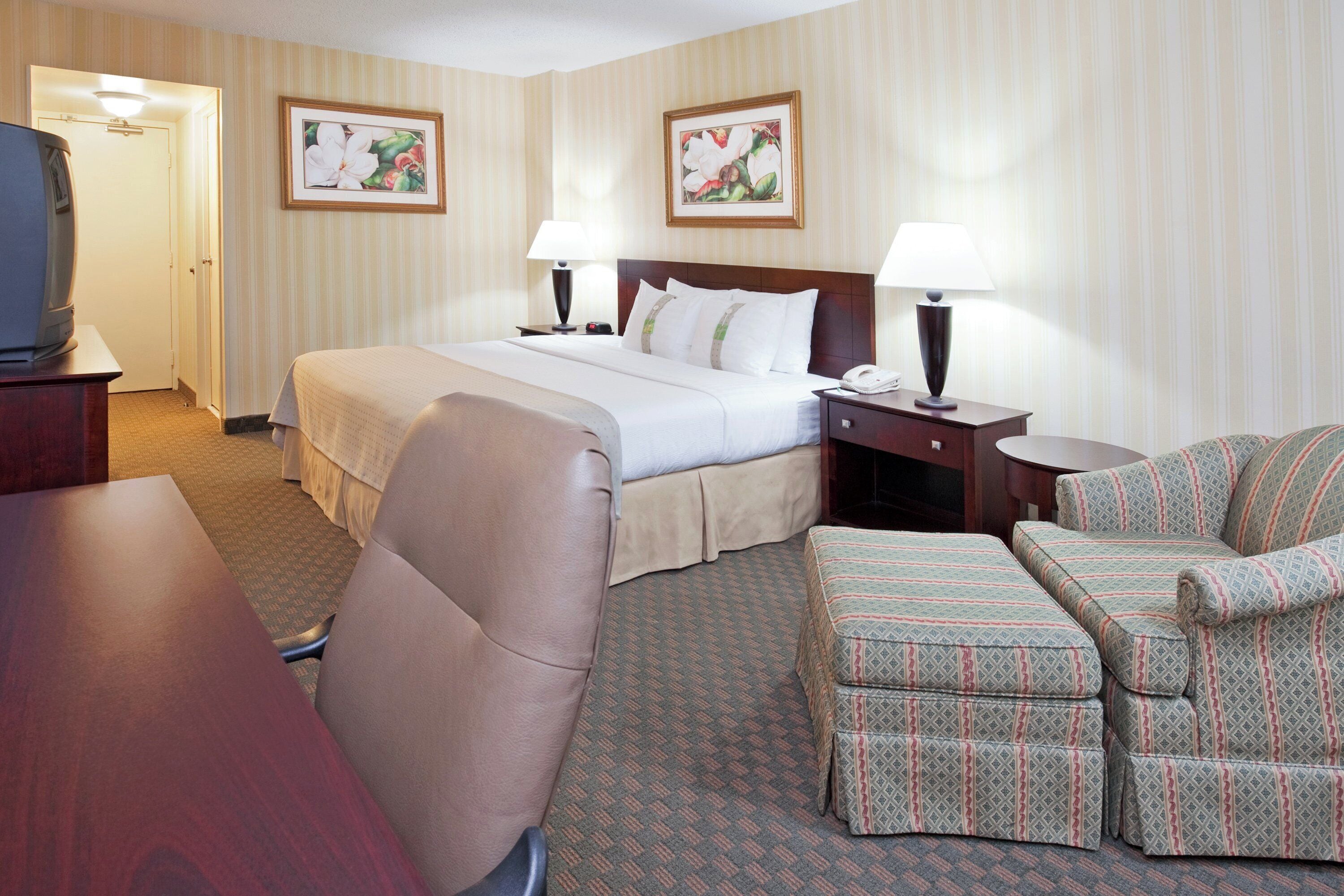 A hotel room with a bed, two bedside tables, a desk, a chair, and a sofa.