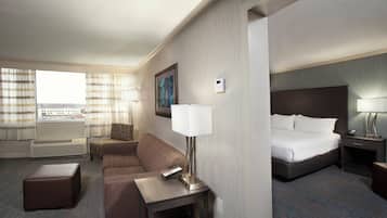 Una habitación de hotel con una cama, un sofá, una mesita con una lámpara, una mesita de noche con lámpara, una ventana con cortinas y vistas a la ciudad.