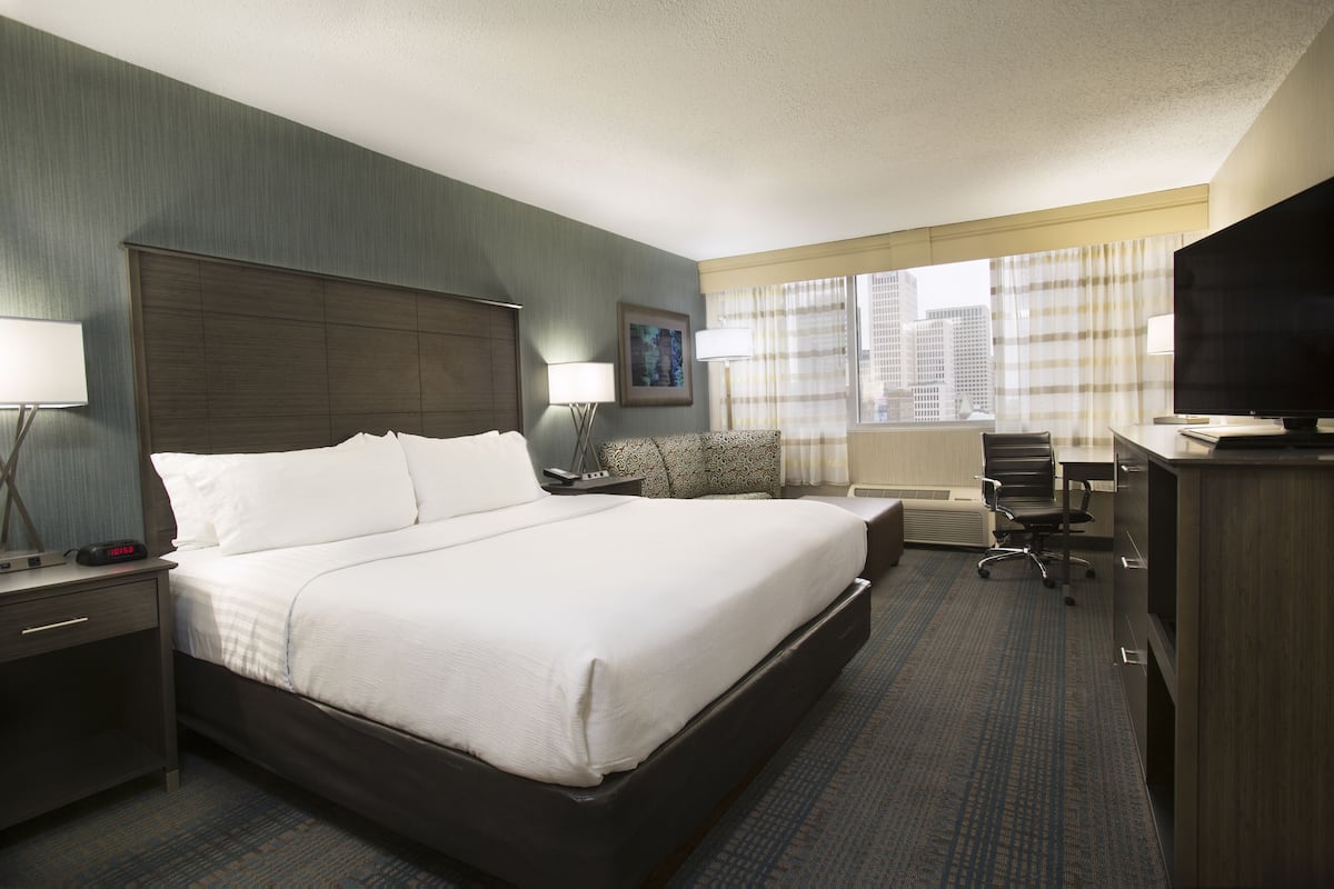 A hotel room with a large bed, a desk with a chair, a television, and a window with curtains.