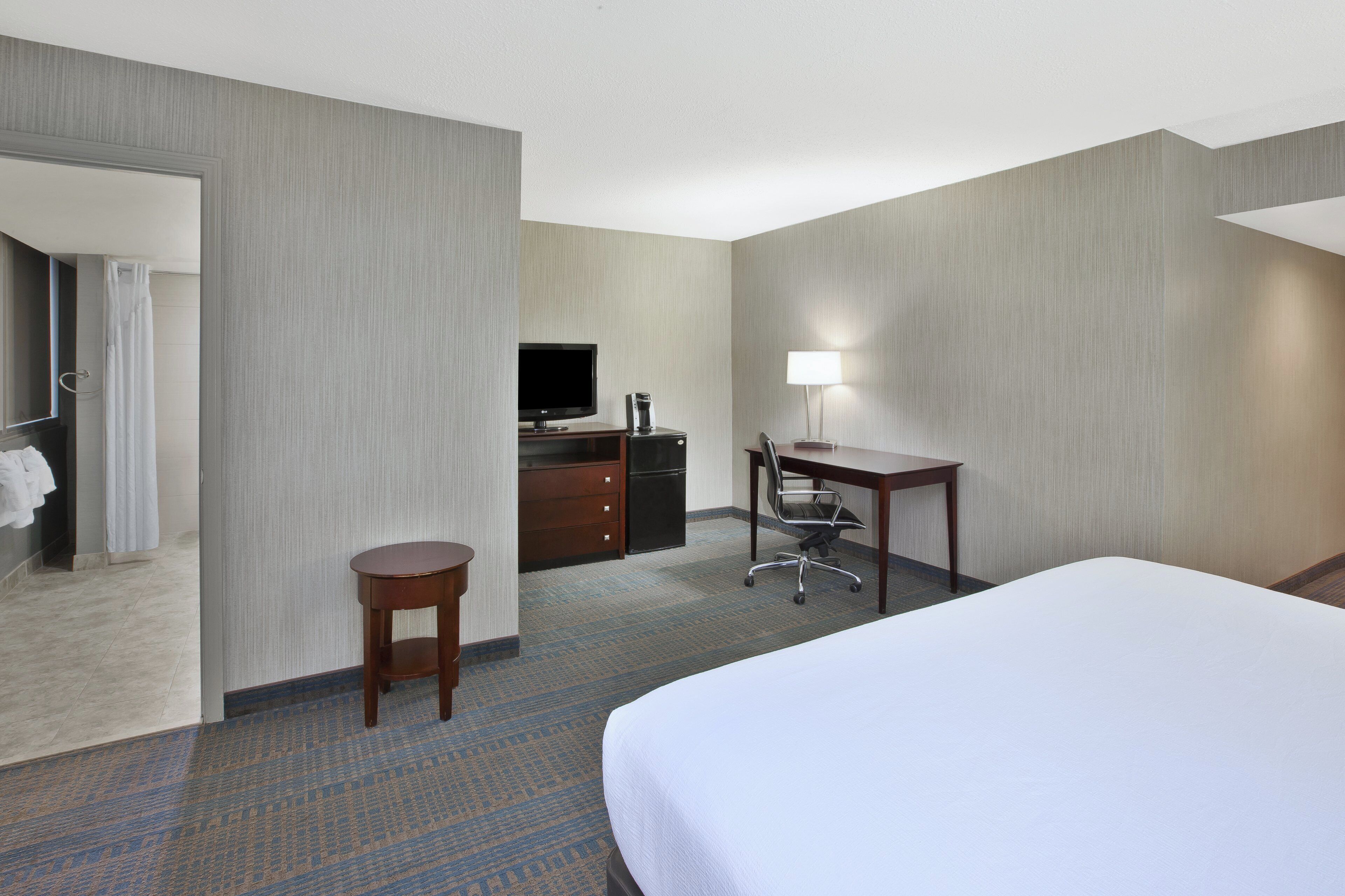 Una habitación de hotel con cama, escritorio, silla, televisor y una mesita.