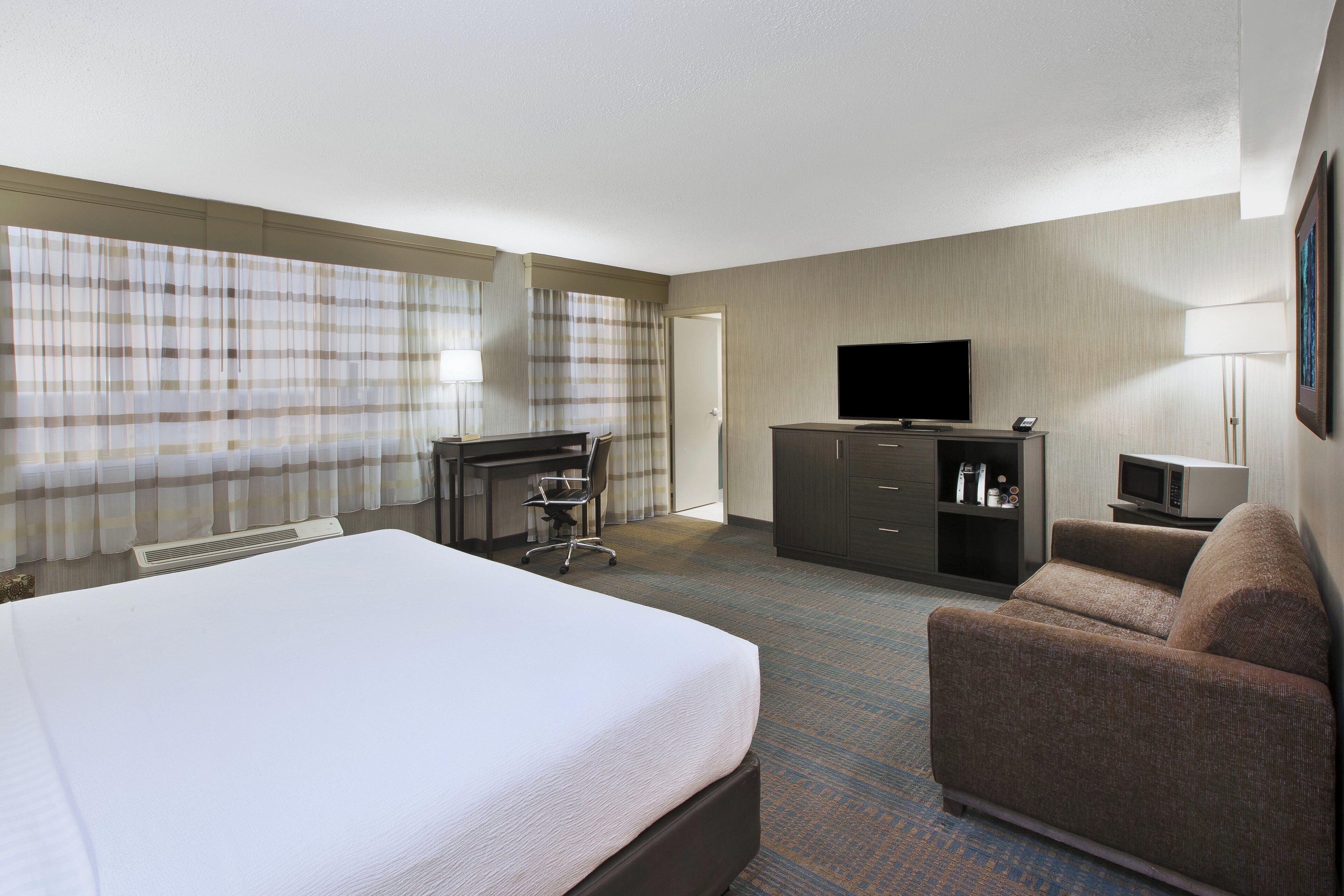 Habitación de hotel con cama, escritorio, televisor, sofá y espejo.