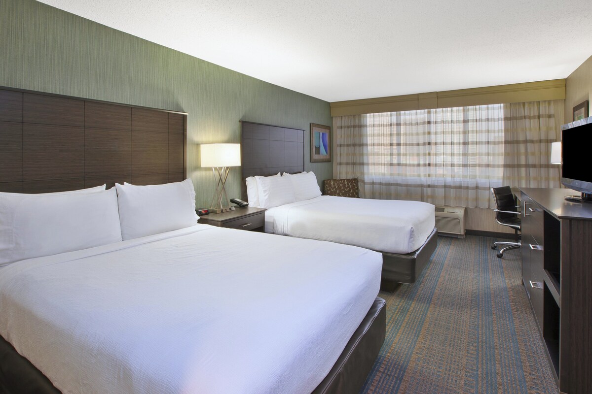 A hotel room with two beds, a desk, a chair, a television, and a window with curtains.