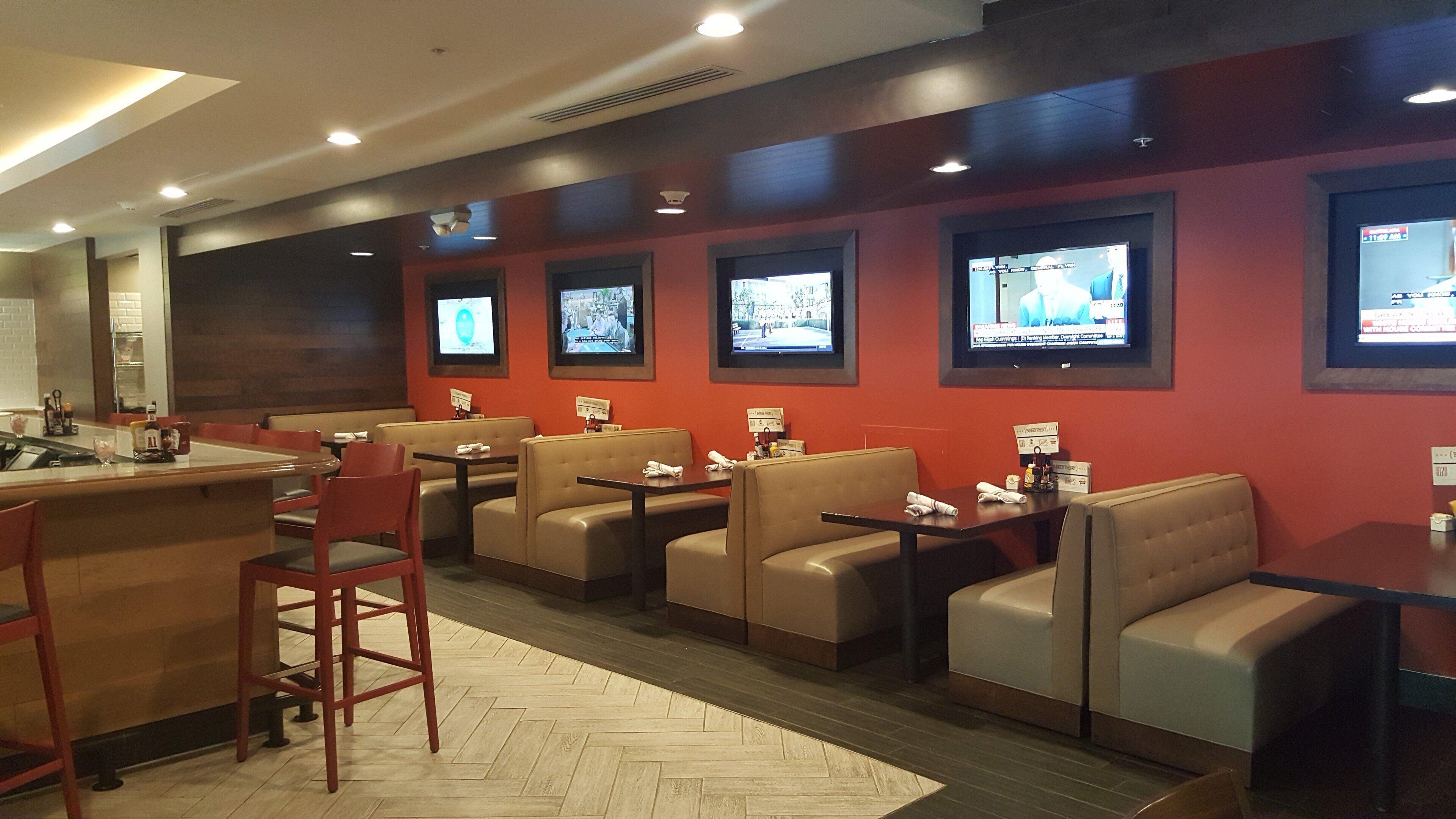 Un restaurante con cabinas y mesas, una zona de bar y varias televisiones en la pared.