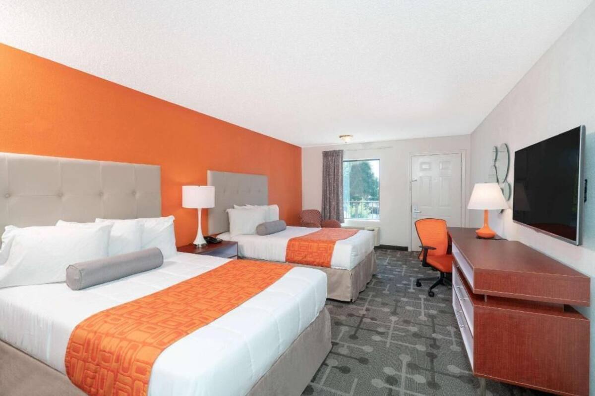 Une chambre d’hôtel avec deux lits, un bureau, une chaise, une télévision et une fenêtre.