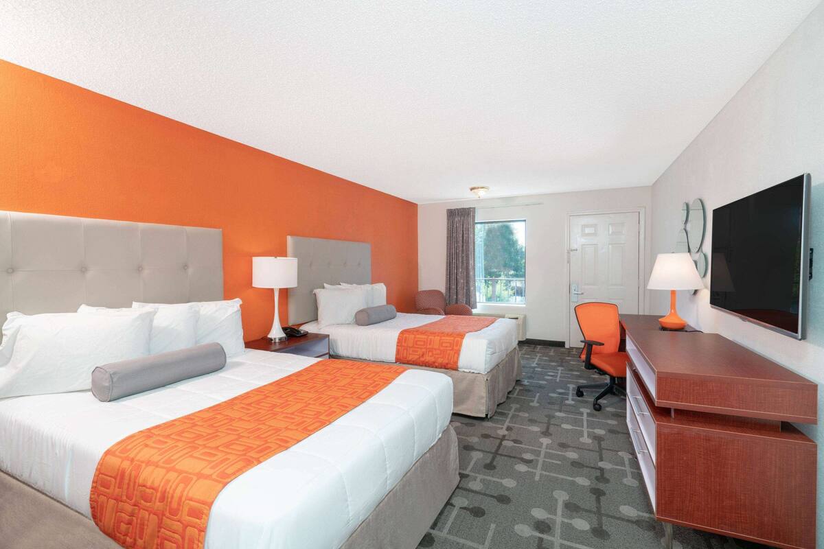 Une chambre d’hôtel avec deux lits, un bureau, une chaise et une télévision.
