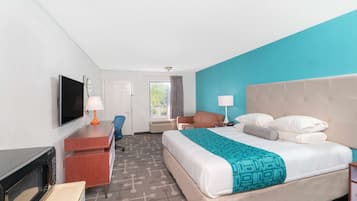 Een hotelkamer met een bed, een bureau met een computer, een televisie en een magnetron.