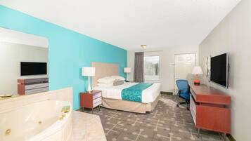 Quarto de hotel com uma cama grande, escrivaninha, televisão, banheiro com banheira e janela com cortinas.