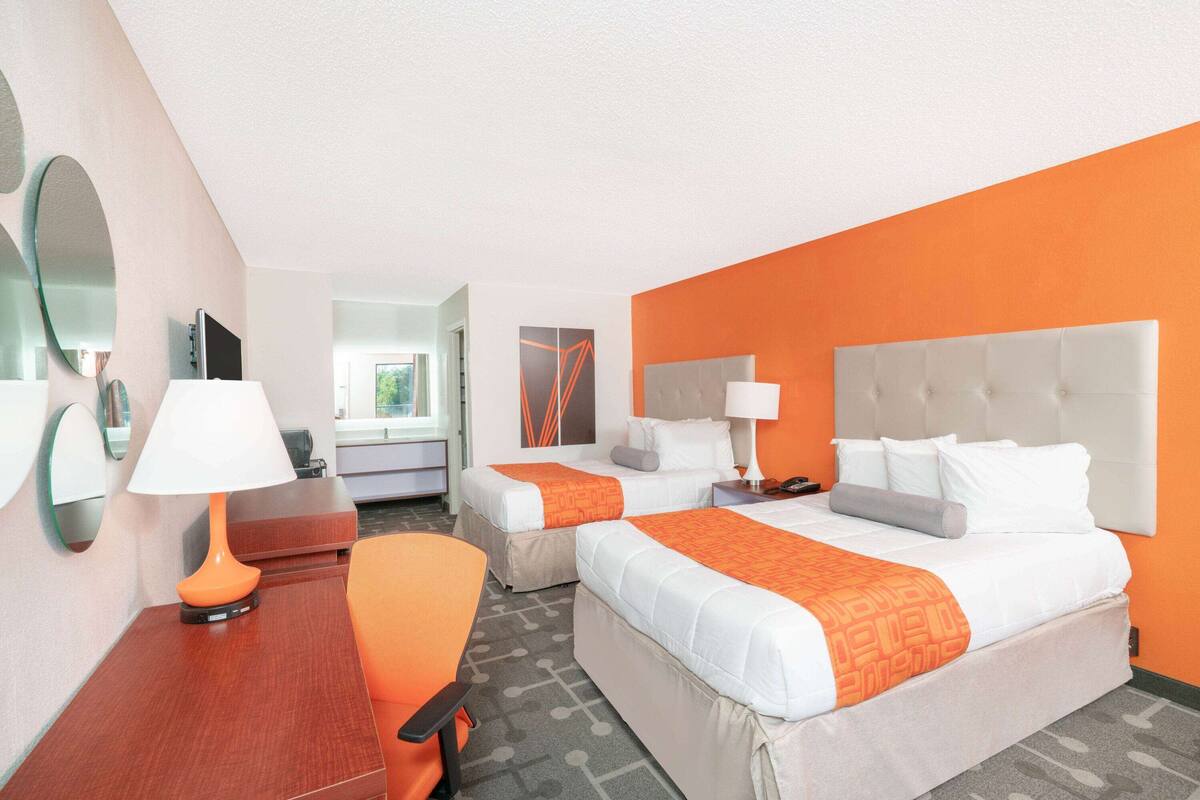 Une chambre d’hôtel avec deux lits, un bureau, une chaise, une lampe et un miroir.
