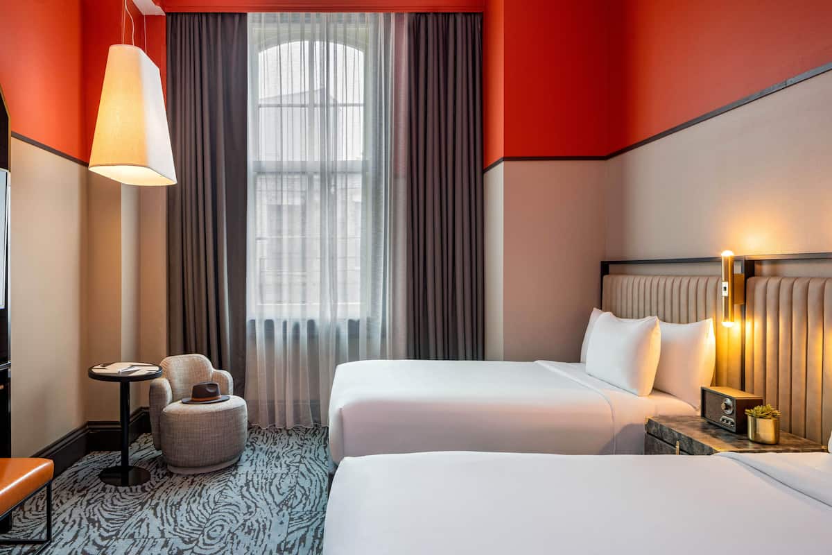 A hotel room with two beds, a TV, a lamp, a small table, and a chair.