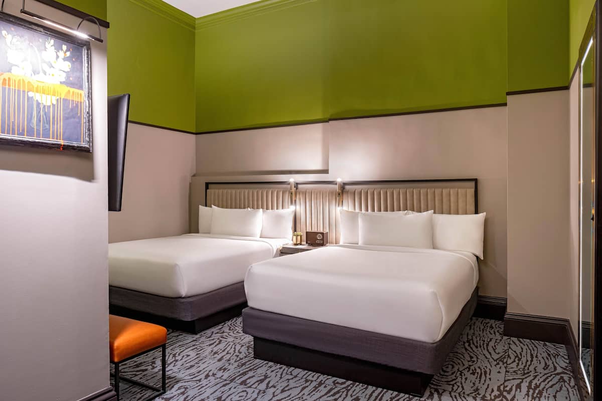 A hotel room with two beds, a small table, a chair, a framed picture, and a mirror.