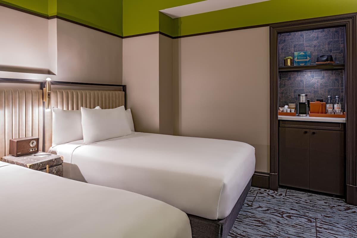 A hotel room with two beds, a minibar, and a small seating area.