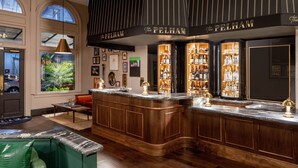A bar area with wooden bar counters, shelves of bottles, and a green leather chair.