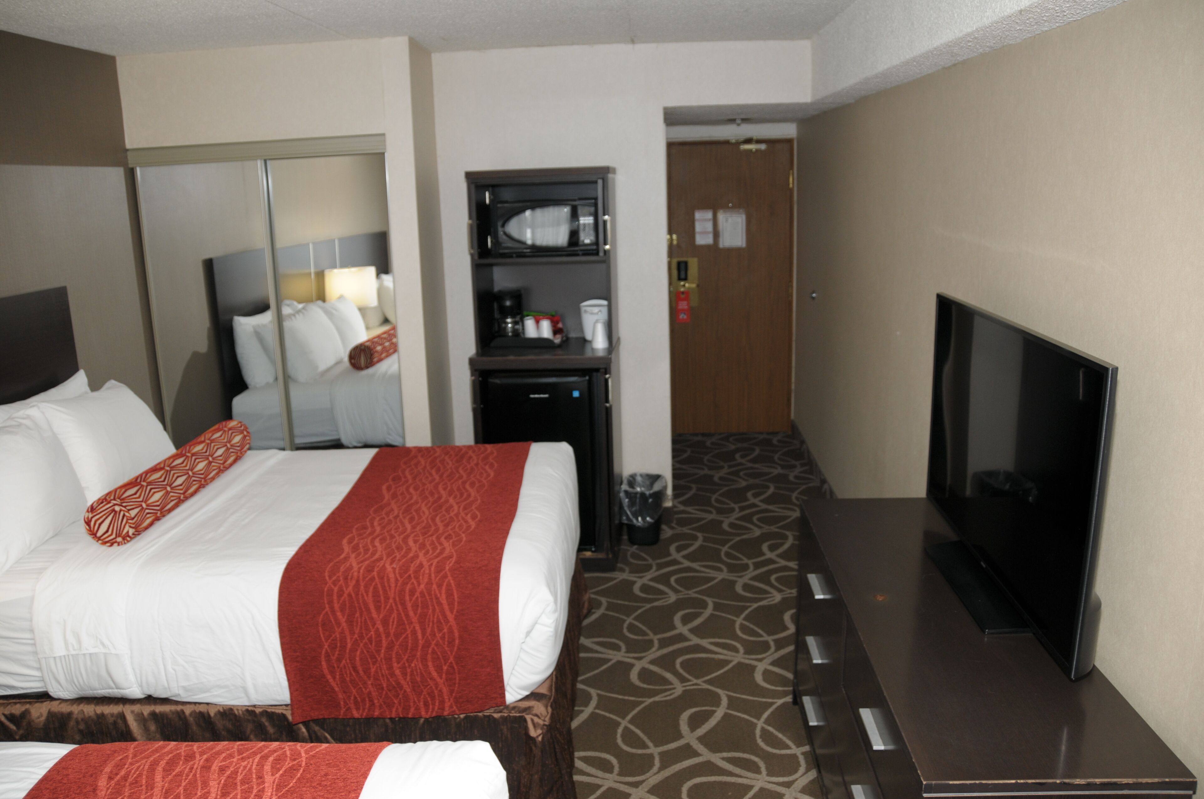 A hotel room with a bed, a TV, a minibar, and a bathroom door.