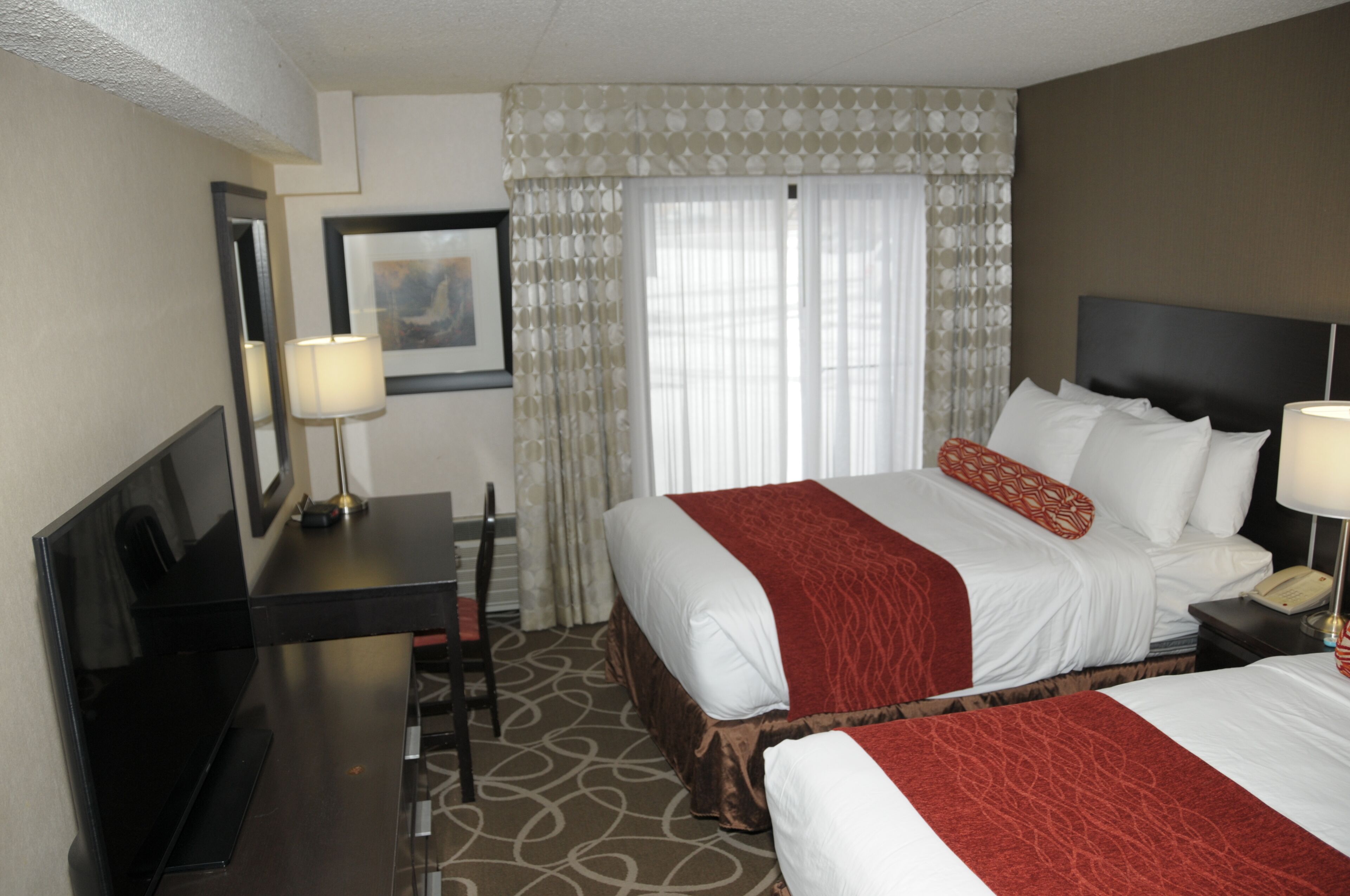 Habitación de hotel con una cama grande, un escritorio con lámpara, una silla y un televisor.