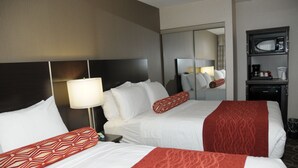 A hotel room with two beds, a nightstand, a lamp, a mirror, and a minibar.