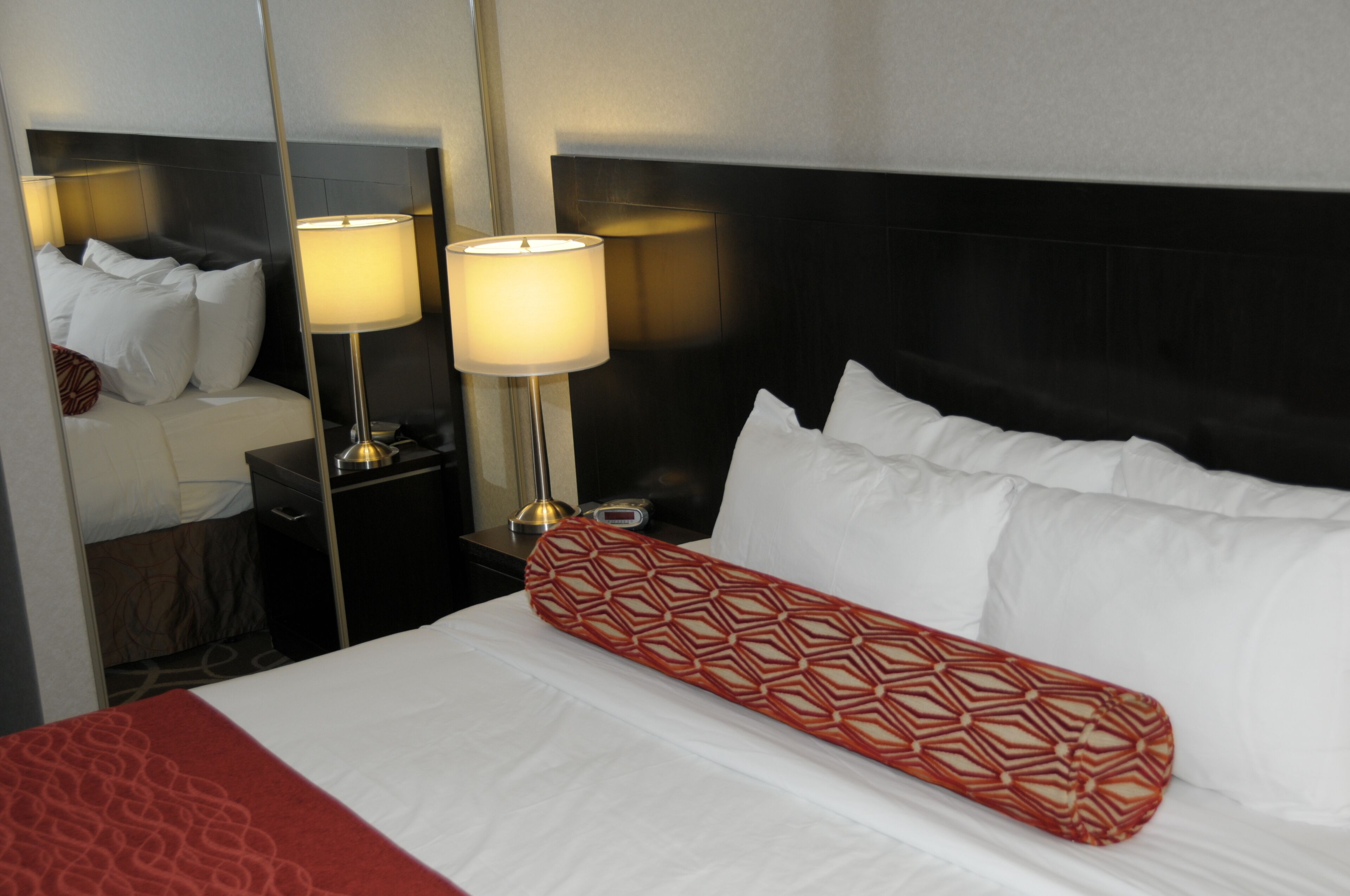 Una habitación de hotel con una cama bien hecha, dos lámparas de noche, una mesita de noche y un espejo.