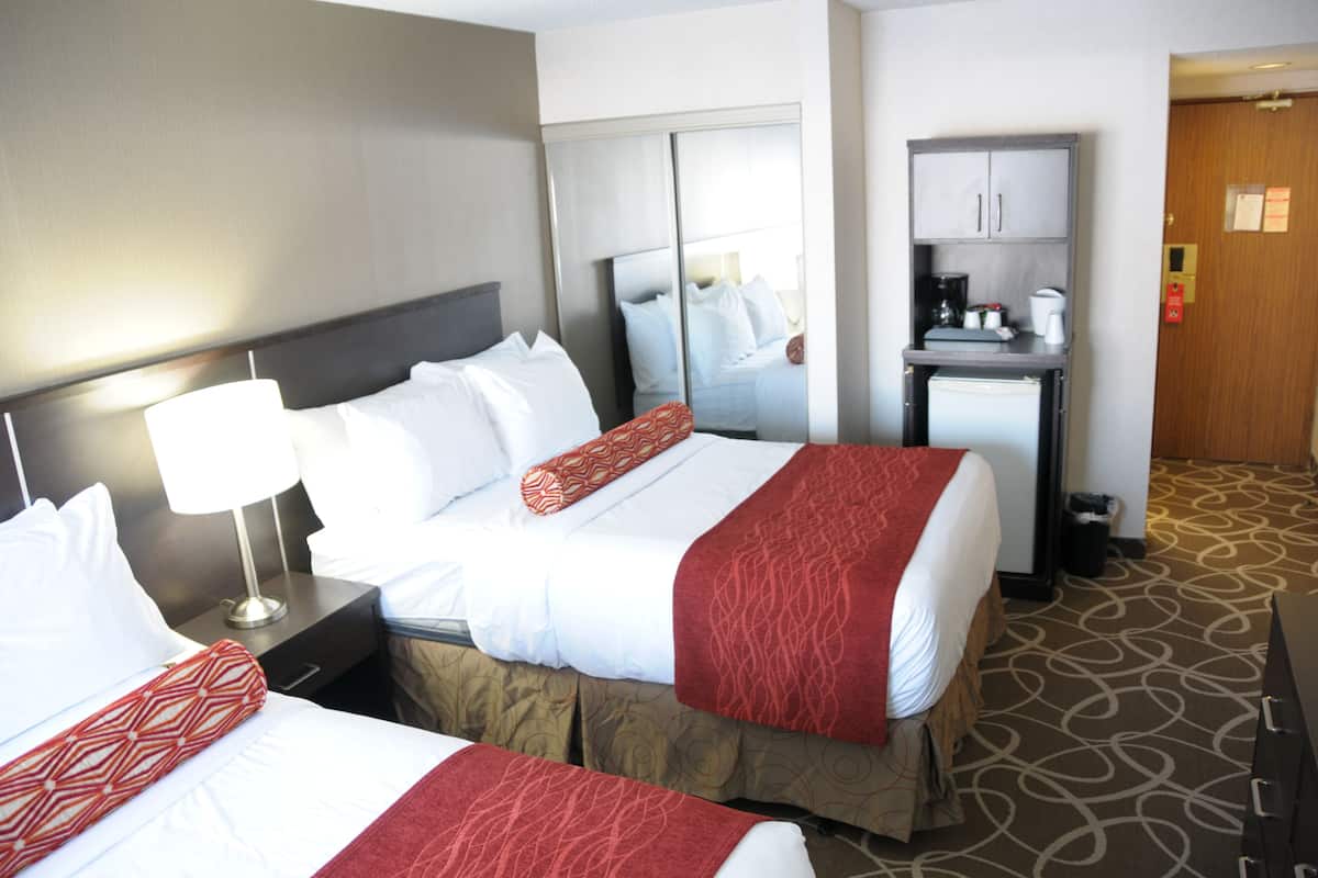 A hotel room with two beds, a desk, a mirror, and a wardrobe.